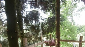 Un espacio de comedor al aire libre con una mesa redonda y sillas, rodeado de árboles y una terraza de madera.