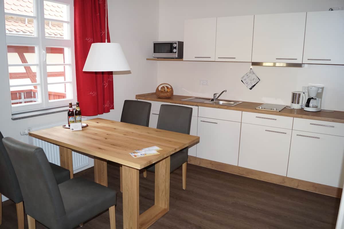A compact kitchen with white cabinets, a wooden dining table, and a red curtain.