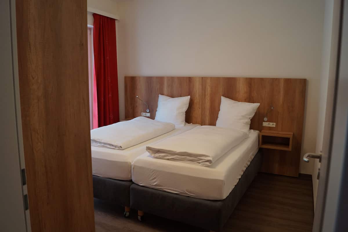 A double bed with a wooden headboard, a bedside table, and a red curtain.