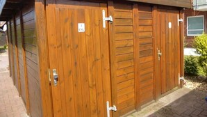 Un bâtiment en bois avec un toit en pente, une porte en métal portant une plaque numérotée et un mur en briques.