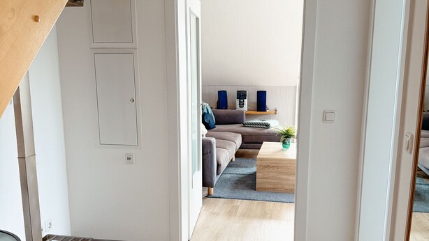 Un intérieur moderne comprenant un escalier, un espace de vie avec un canapé et une table basse, et un couloir menant à une autre pièce.