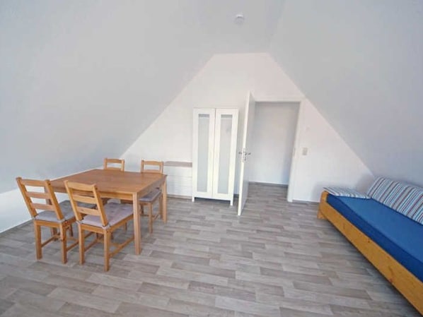 A room with a wooden dining table and chairs, a sofa, and a door leading to another room.