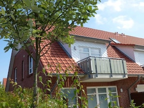 A two-story house with a red-tiled roof, a balcony, and a garage door.