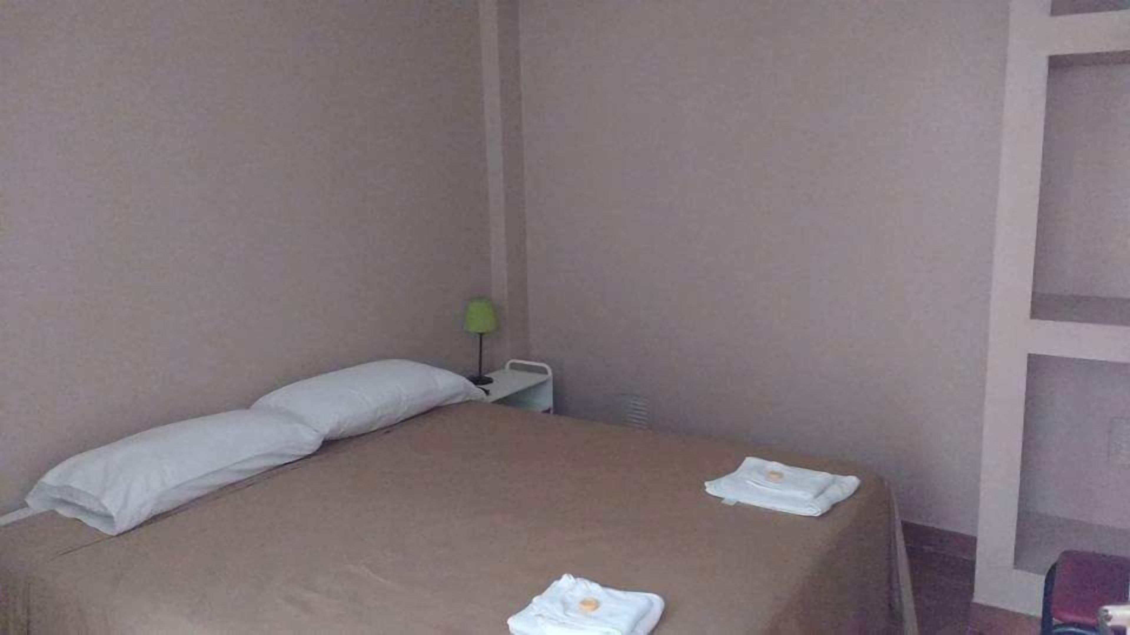 A single bed with a beige bedspread, a white pillow, and two folded towels on the bed.