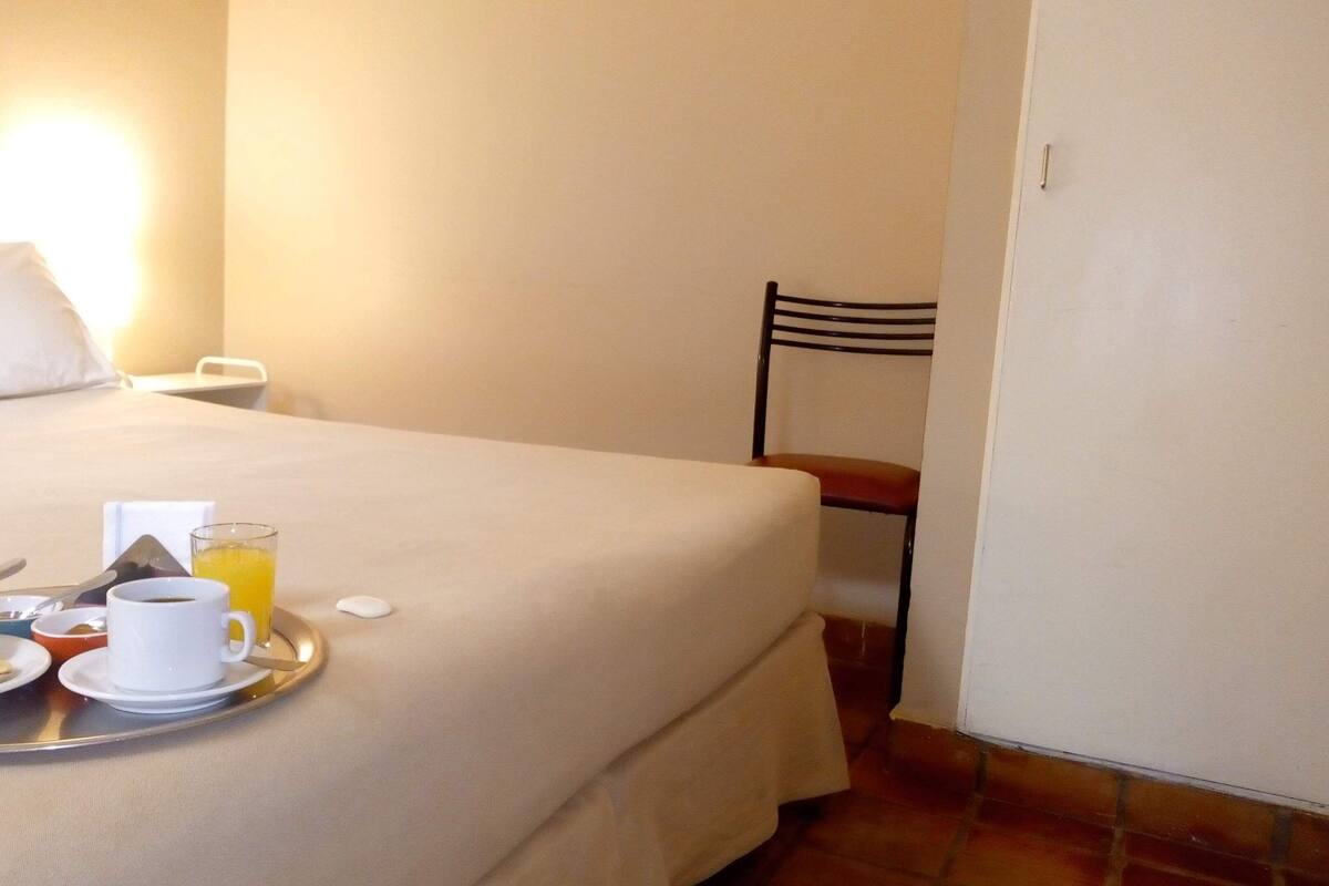 Un lit bien fait, avec un plateau contenant des croissants, une tasse de café et un verre de jus d’orange.