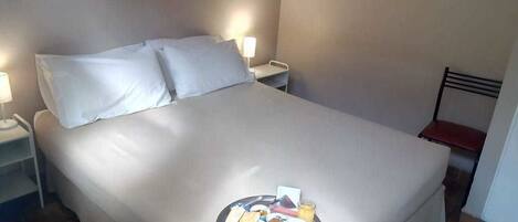A neatly made bed with a tray of breakfast items, including toast, coffee, and juice, in a hotel room.