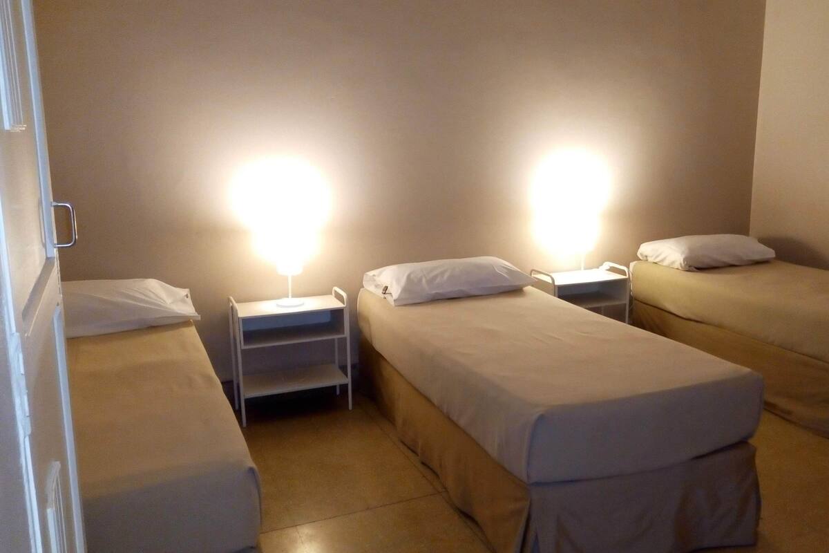 Une chambre d’hôtel avec deux lits simples, chacun doté d’une table de chevet et d’une lampe, ainsi qu’une petite étagère.