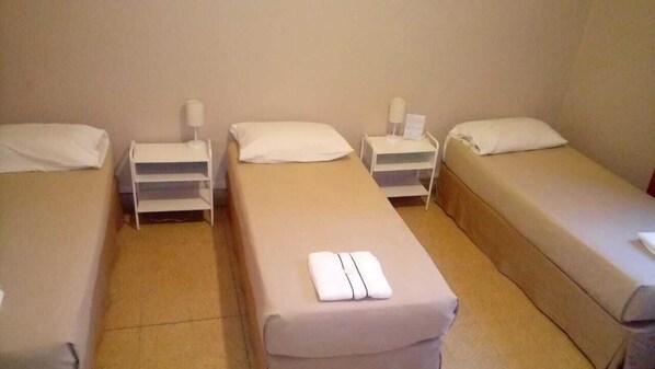 Une chambre avec trois lits simples, chacun doté d’un matelas et d’un oreiller blancs, ainsi que de tables de chevet avec des lampes.