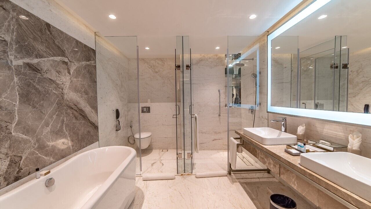 Un baño moderno con pared de mármol, ducha con cerramiento de vidrio, bañera independiente y un espejo grande.