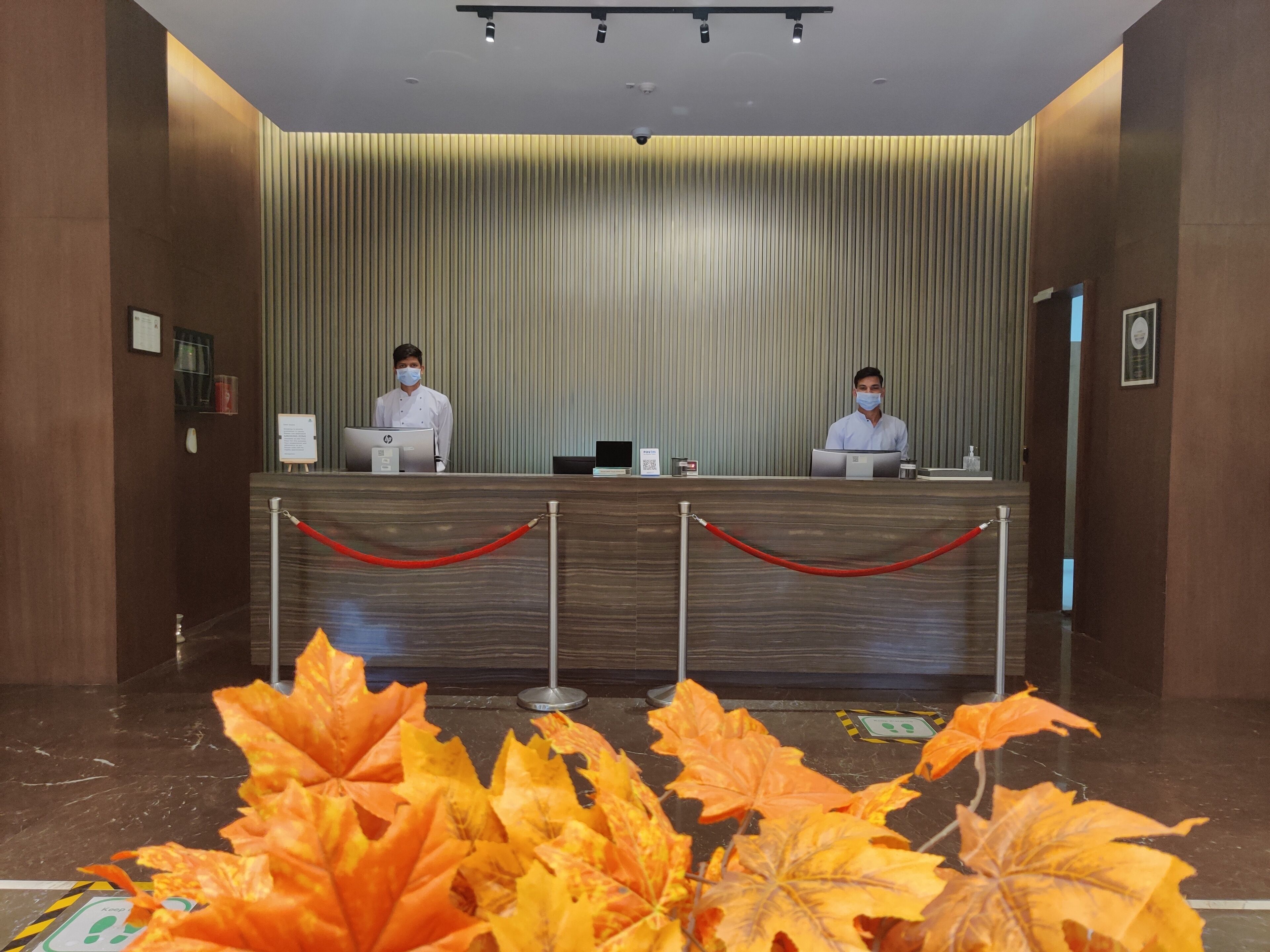 A reception desk with two staff members, a red rope barrier, and autumn leaves in the foreground.
