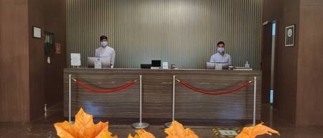 A reception desk with two staff members, a red rope barrier, and autumn leaves in the foreground.