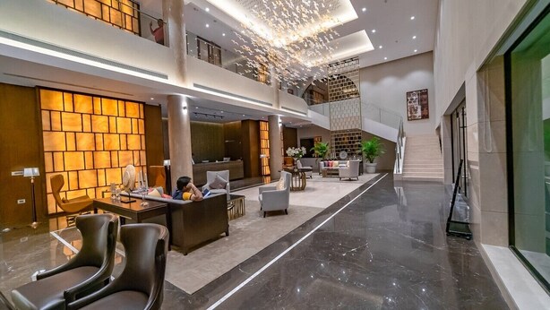 Un moderno vestíbulo de hotel con un mostrador de recepción, una zona de estar y una escalera que sube a un nivel superior.
