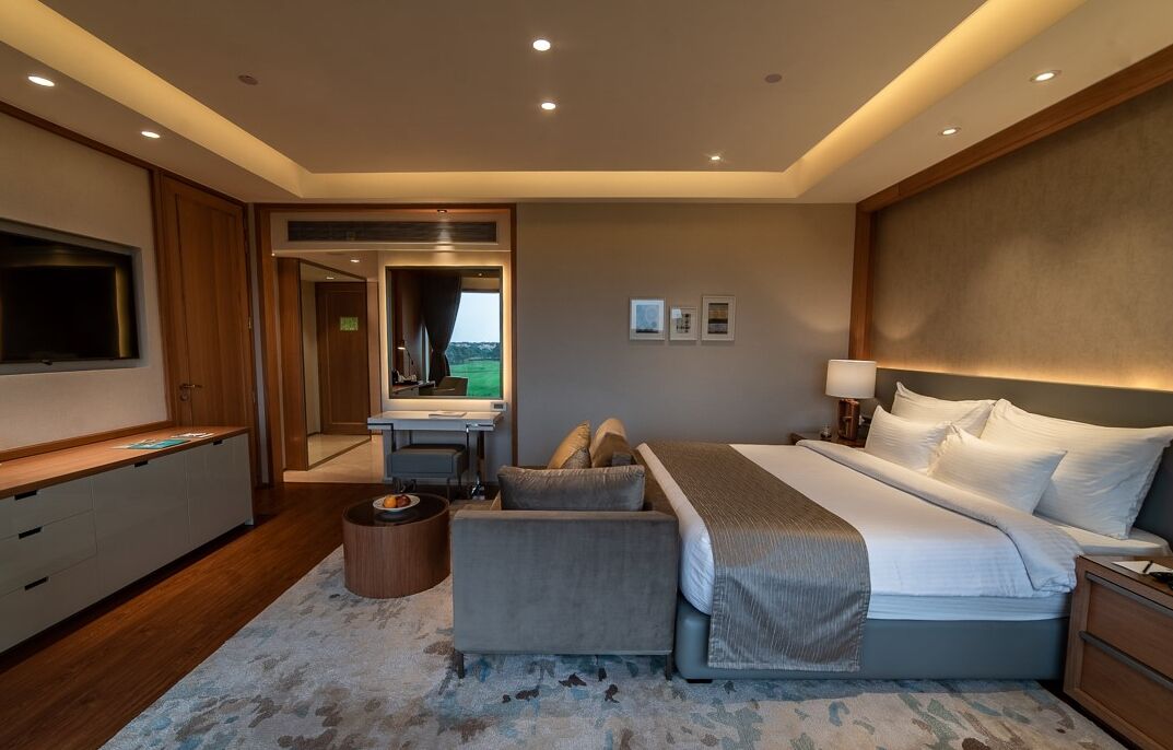 A modern hotel room with a large bed, a desk, a television, and a view of the outdoors.