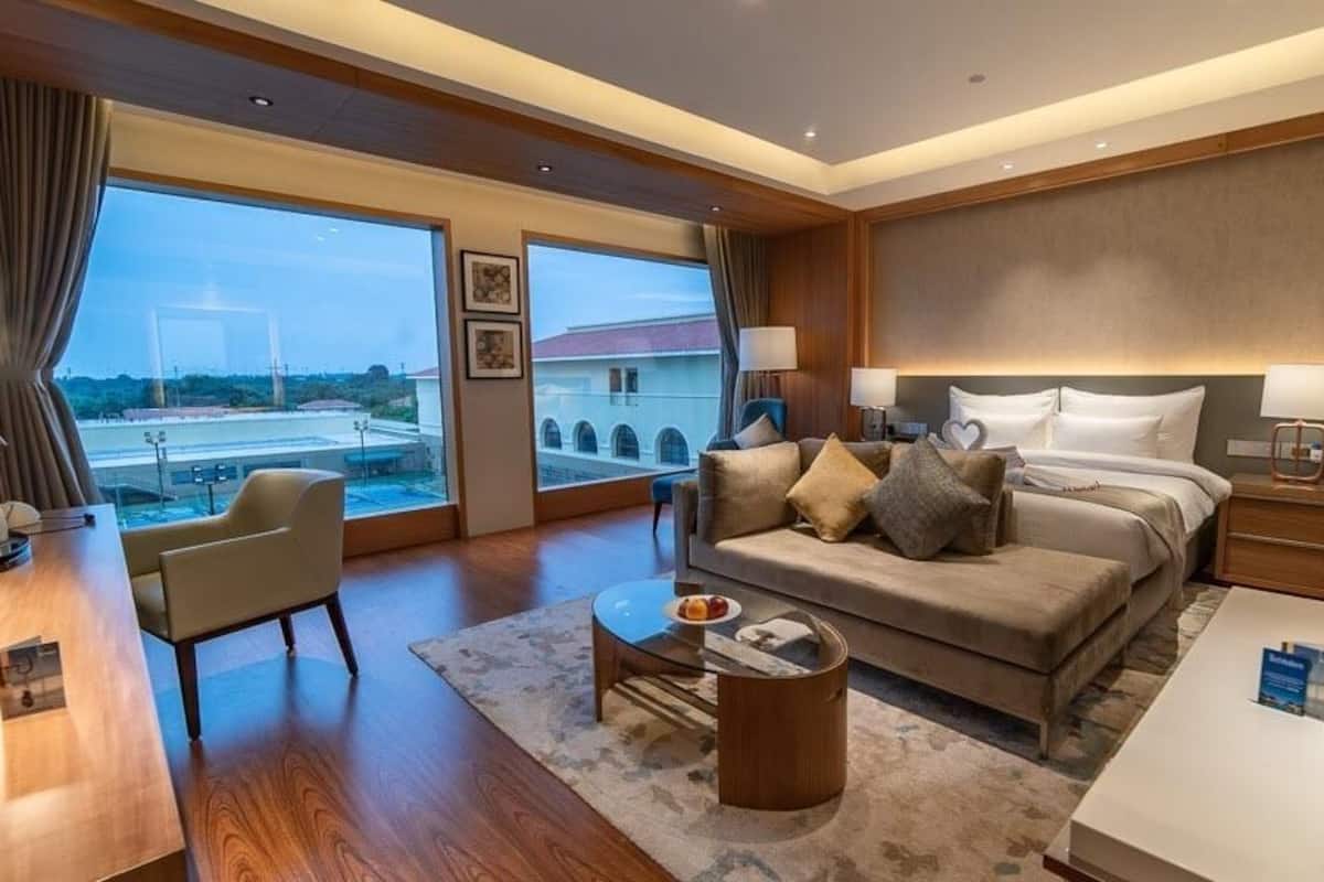 A hotel room with a large window, a sofa, a coffee table, a desk, and a bed.