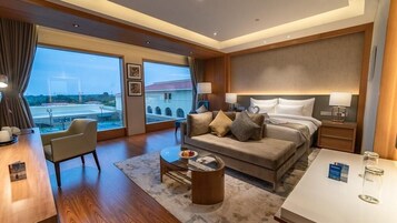 A hotel room with a large window, a sofa, a coffee table, a desk, and a bed.