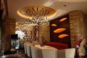 A modern hotel lobby with a central seating area, a decorative light fixture, and a reception desk.