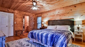 Ein Schlafzimmer in einer Holzhütte mit Bett, Nachttisch und Deckenventilator.