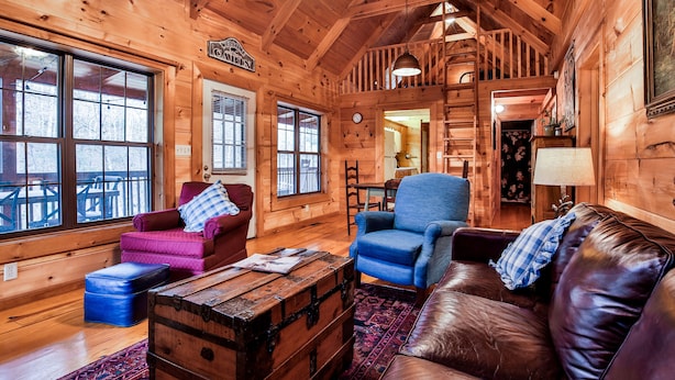Ein gemütliches Blockhaus-Interieur mit Holzwänden, einem Ledersofa, einem blauen Sessel und einer Holzbank.
