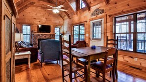 Ein Interieur einer Holzhütte mit Esstisch, Stühlen, einer Couch und einem Kamin.
