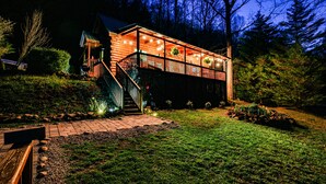 Eine Blockhütte mit Veranda und Sitzbereich im Freien, umgeben von einem angelegten Garten und Bäumen.