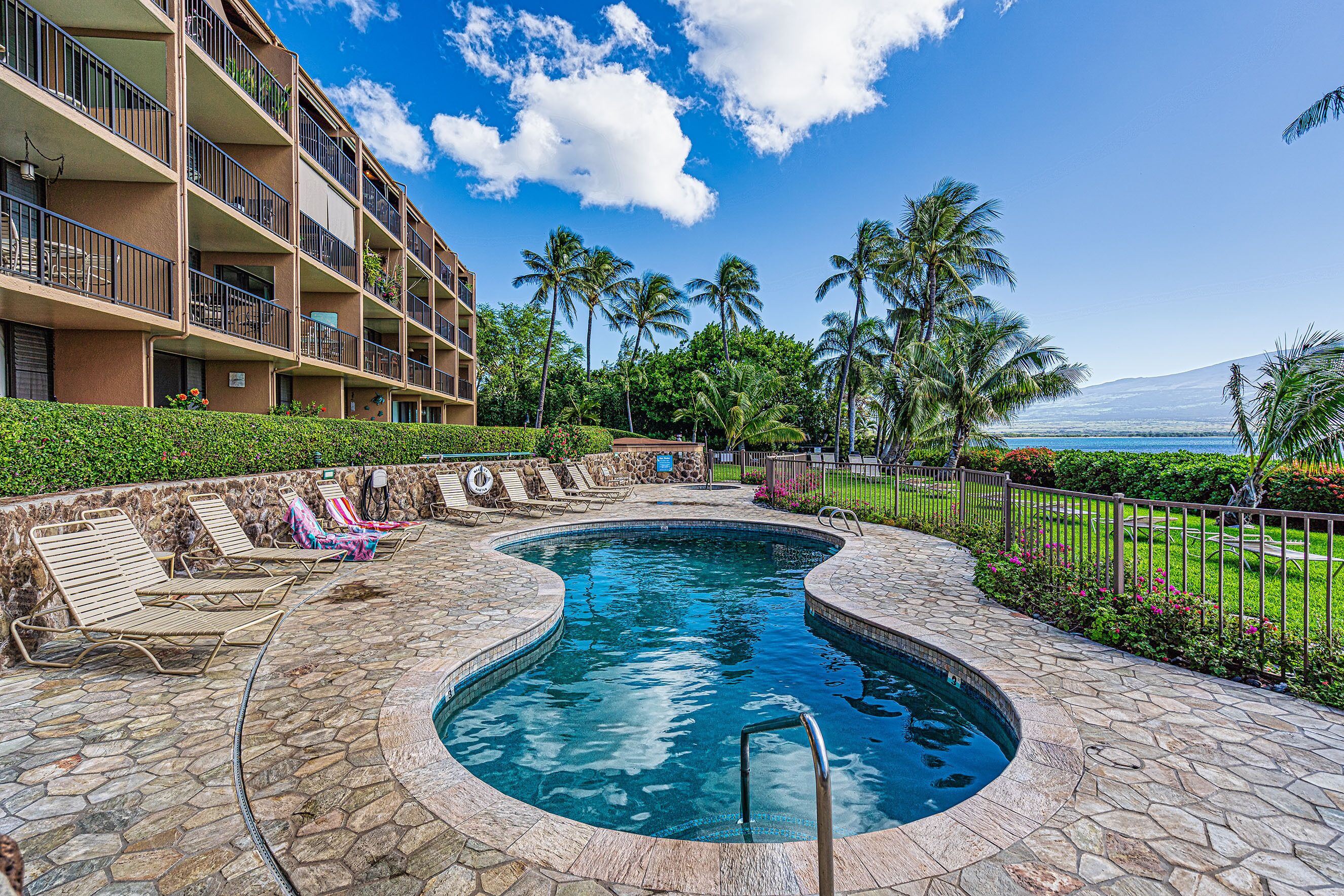 A swimming pool with lounge chairs, a stone deck, and a view of a mountain and ocean.