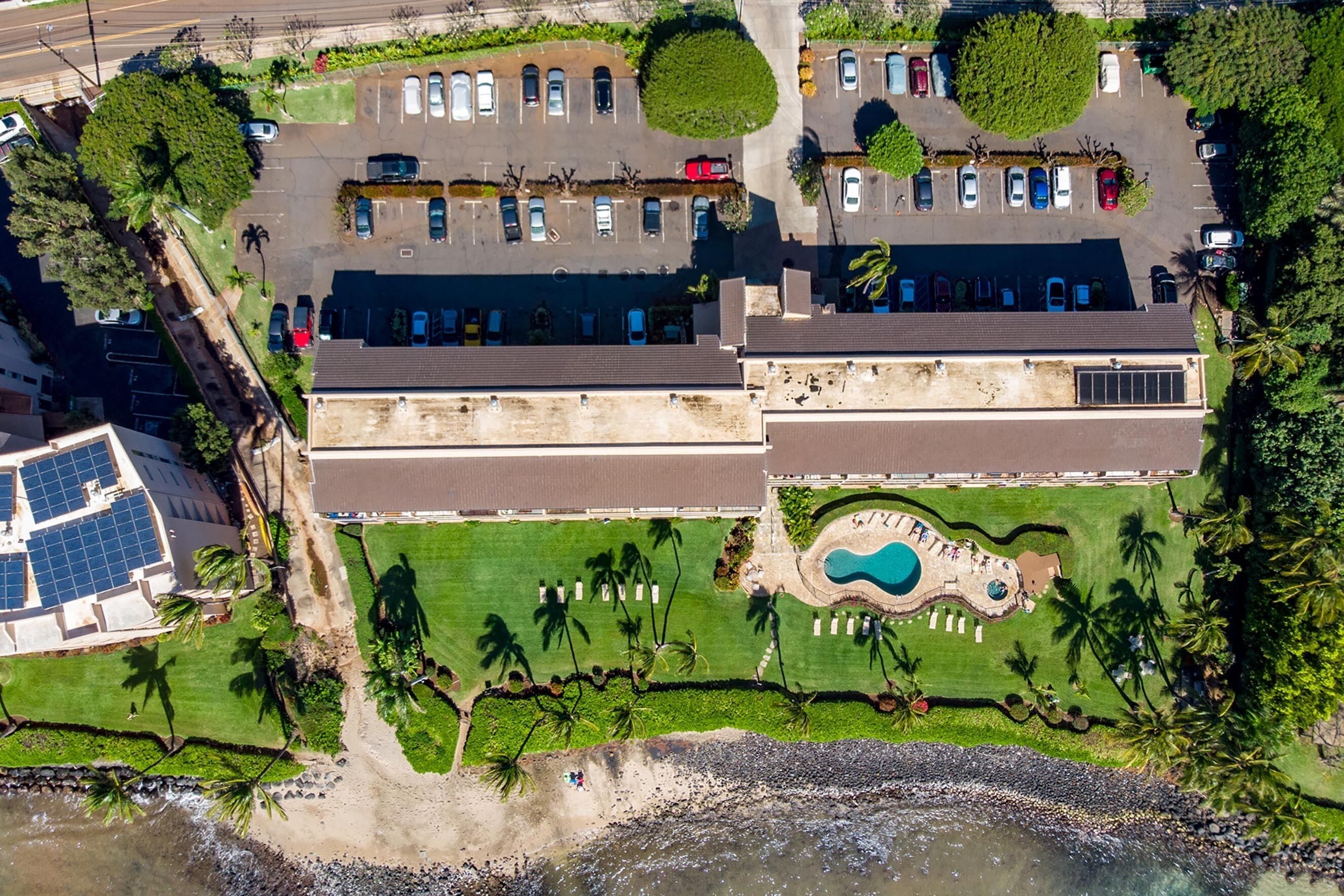 An aerial view of a resort with a swimming pool, parking area, and beachfront.