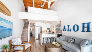 A spacious living area with a kitchen, a staircase, and a large window. - Maalaea Banyans 411 - Modern Renovation, Direct Ocean Front, Incredible View, AC (Wailuku)