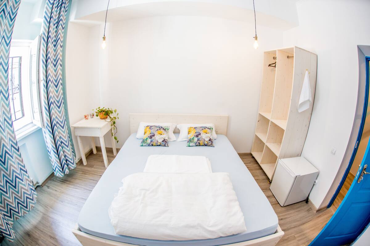A bedroom with a bed, a small desk, a chair, a plant, and a wardrobe.