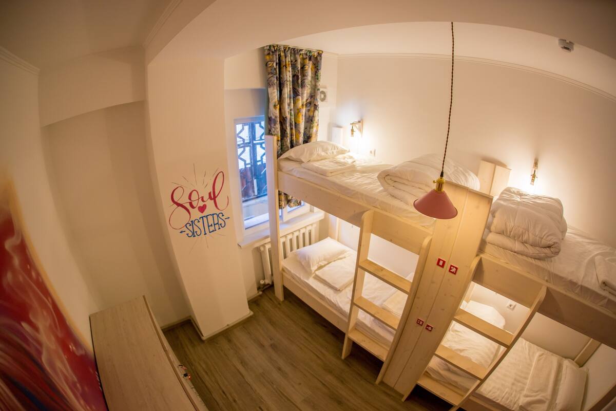 A bunk bed room with a window, a radiator, and a wall with a 'Love Sisters' sign.