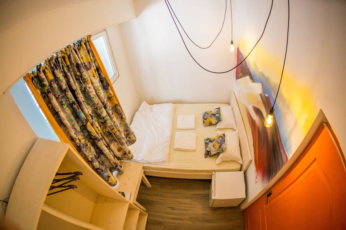 A compact bedroom with a bed, a small wooden shelf, and a window with curtains.