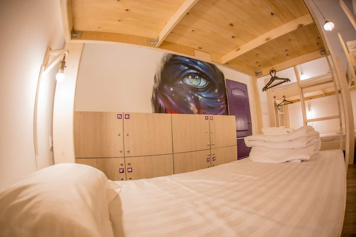A hotel room with a bed, a large wall mural, wooden lockers, and a hanging coat rack.