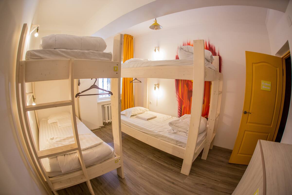 A bunk bed room with a wooden floor, a yellow door, and a small table with a lamp.