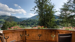 A wooden deck with heart-shaped handles, overlooking a scenic valley with mountains and a village.
