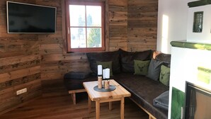 A cozy cabin interior with a wooden wall, a window, a sofa, a table with candles, and a television mounted on the wall.