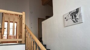 A wooden staircase with a handrail, a white wall with a framed picture, and a window with blinds.