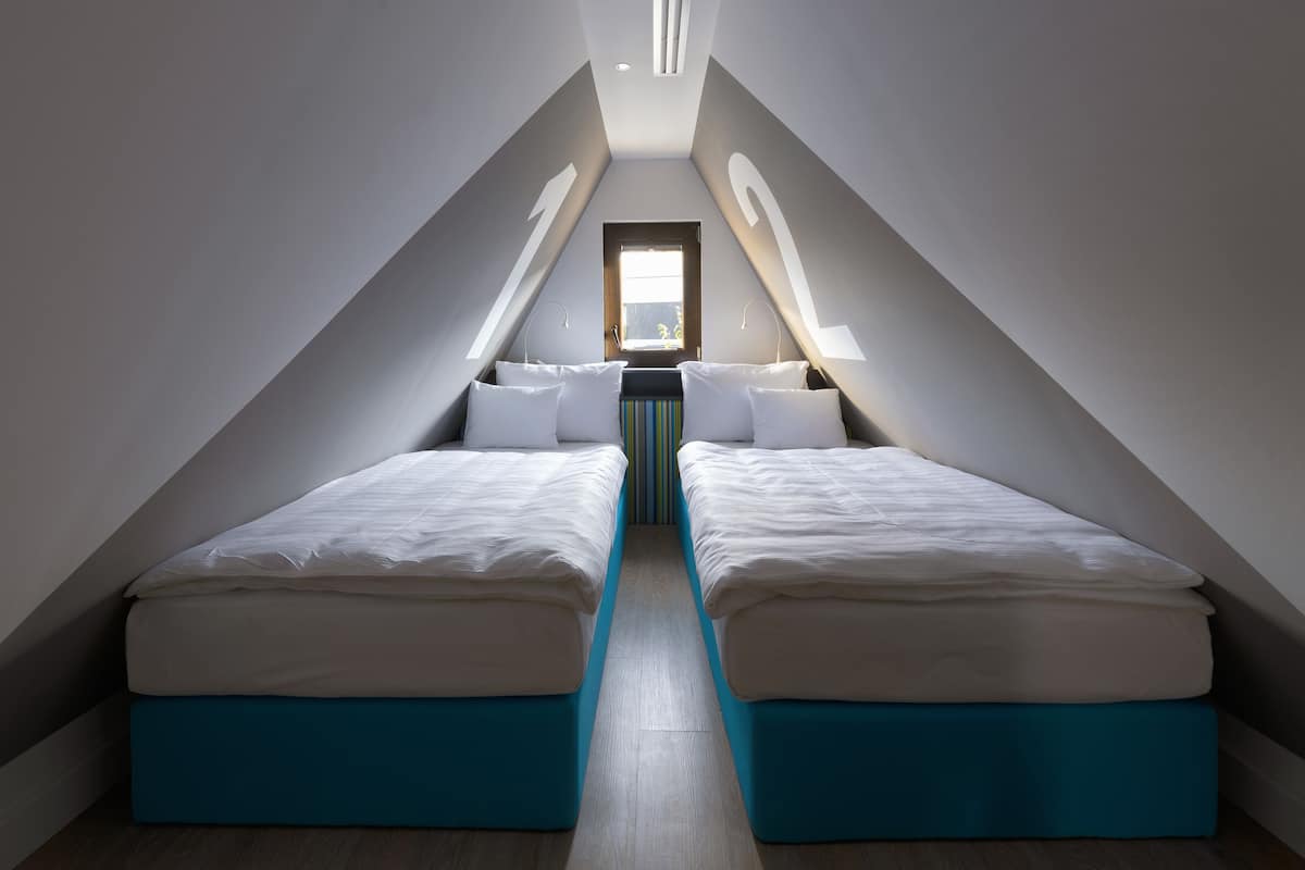 A narrow, high-ceilinged attic bedroom with two beds, a central window, and a skylight.