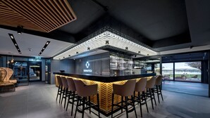 A modern bar area with a geometric ceiling design, bar stools, and a visible exit sign. - Donautica Hotel & Restaurant (Fadd)
