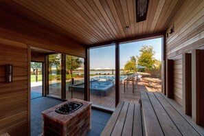 Un espace piscine intérieur moderne, doté d’une terrasse en bois, d’un jacuzzi et de portes vitrées donnant accès à une piscine extérieure.