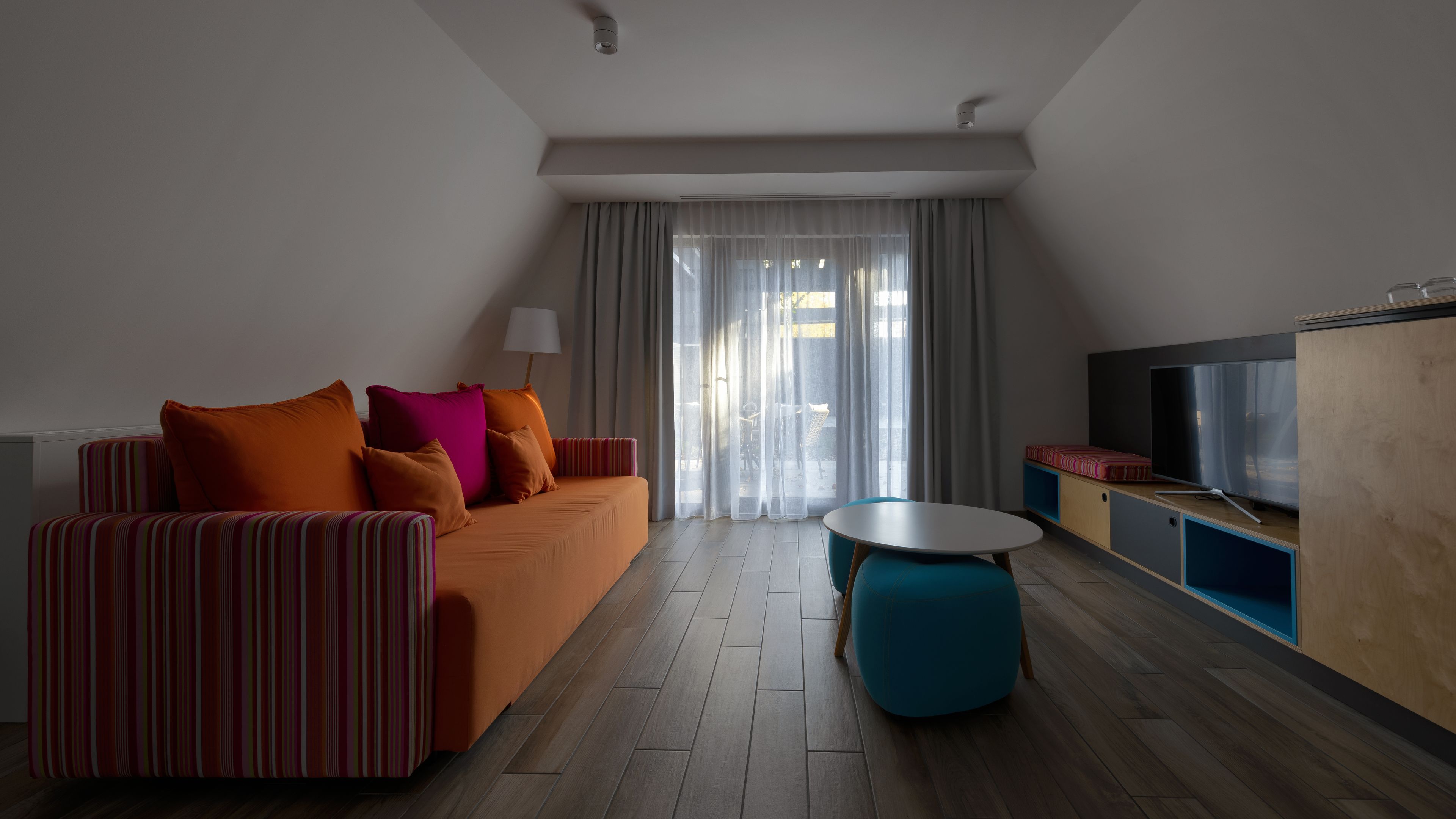 A modern living room with a sofa, ottoman, and a TV on a wooden cabinet.