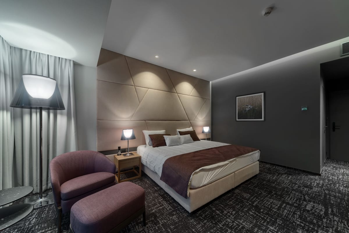 A modern hotel room with a large bed, bedside lamps, a chair, and a floor lamp.