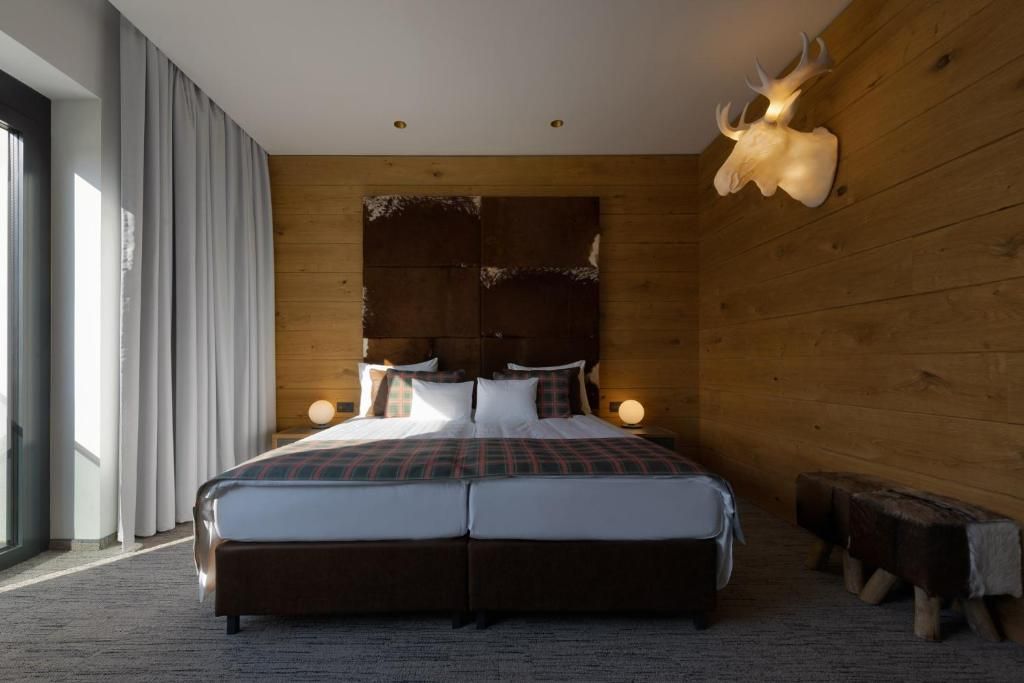 A double bed with a plaid bedspread, wooden headboard, bedside lamps, and a large animal skull mounted on the wall.