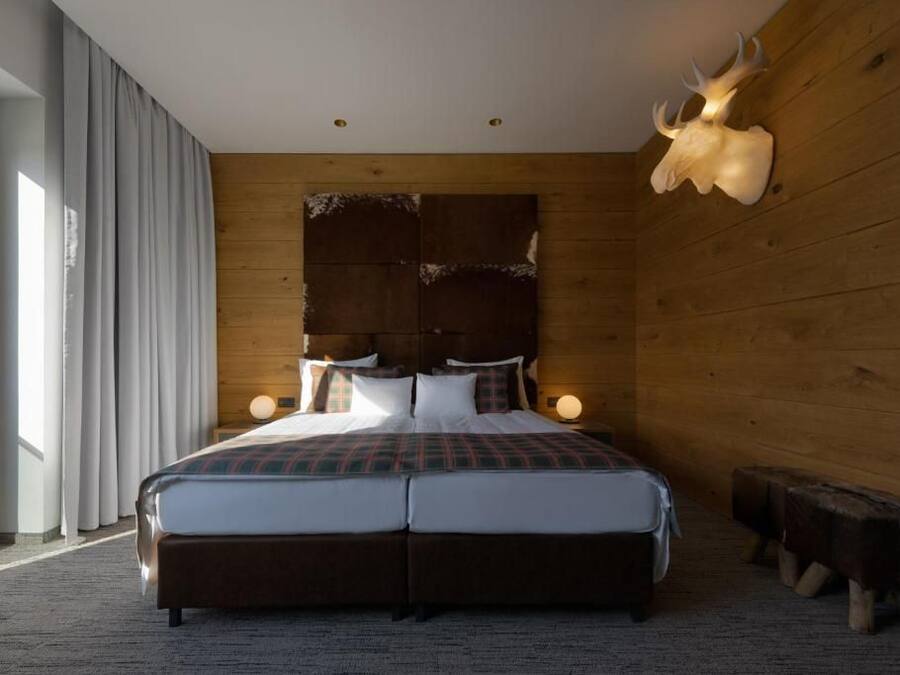 A double bed with a plaid bedspread, wooden headboard, bedside lamps, and a large animal skull mounted on the wall.