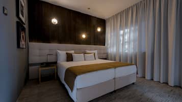 Ein modernes Hotelzimmer mit einem großen Bett, einer Wand mit Holzpaneelen, zwei Nachttischlampen und Blick ins Freie durch transparente Vorhänge.