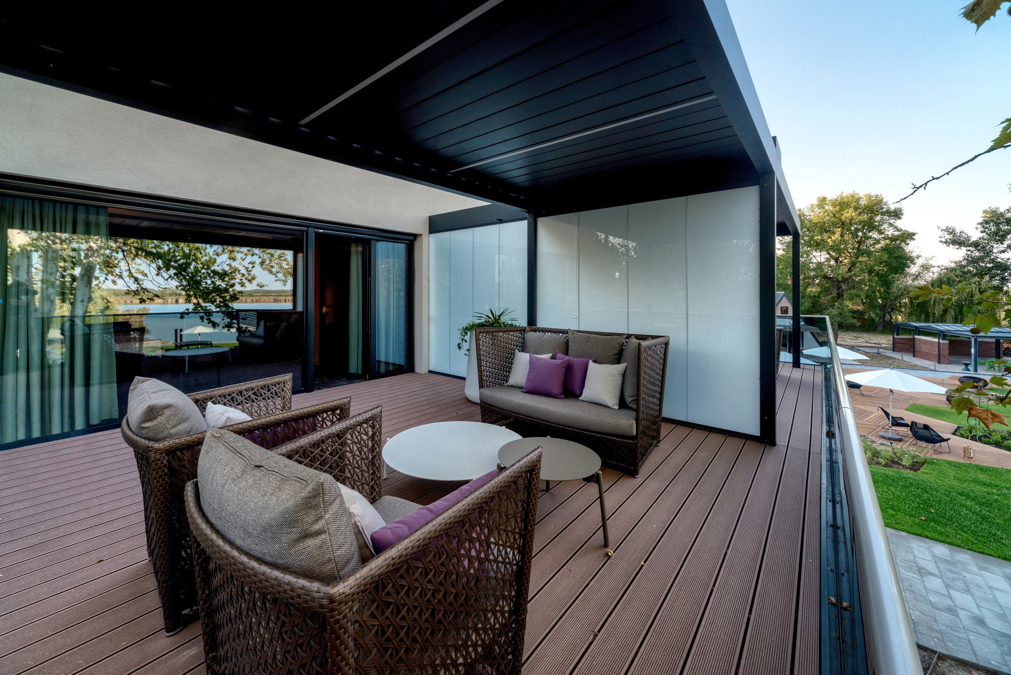 Eine moderne Terrassenanlage im Freien mit Korbmöbeln, einem runden Tisch und einer Couch mit Kissen.