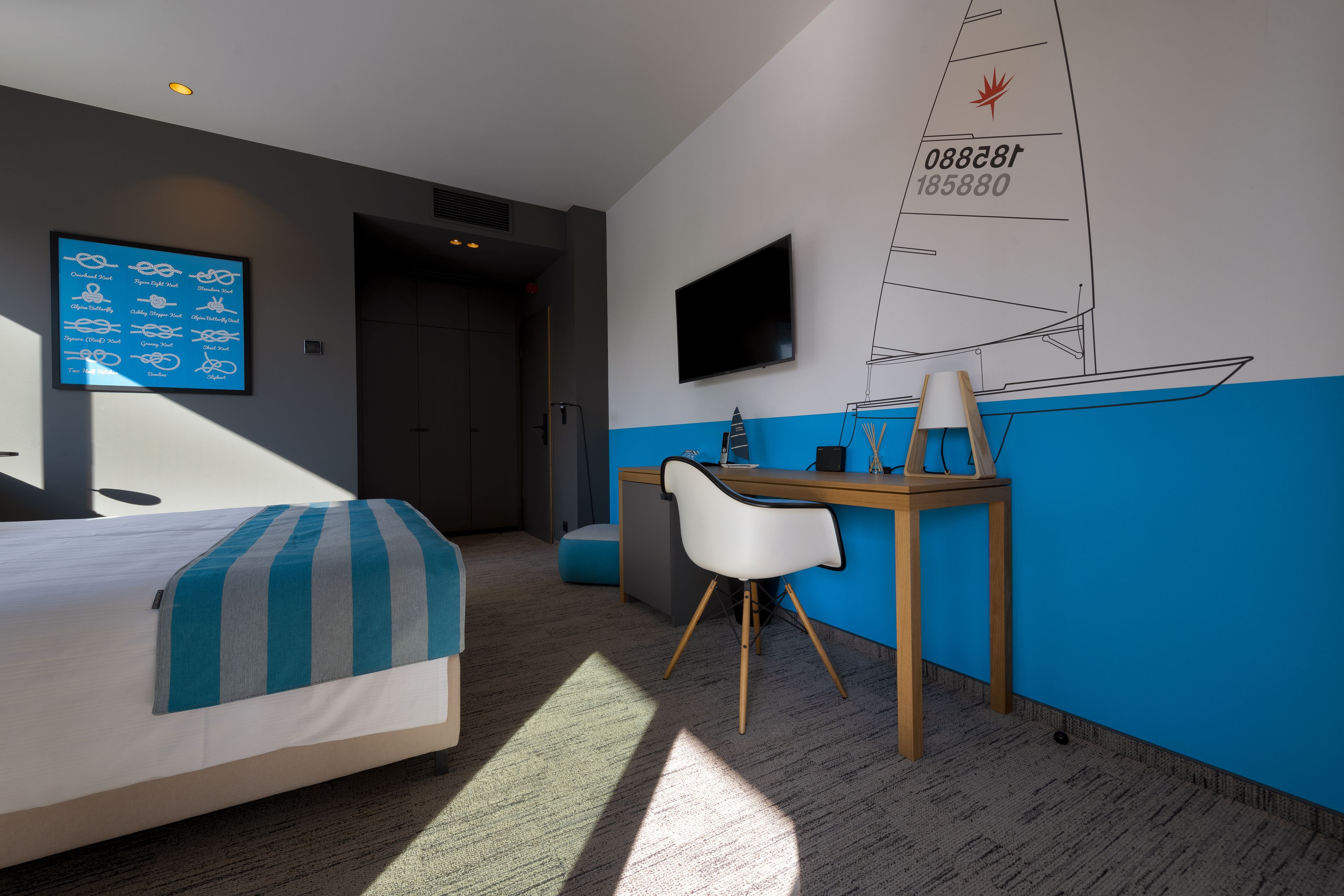 Una habitación de hotel moderna con una cama, un escritorio, una silla, un televisor y un dibujo de un velero en la pared.