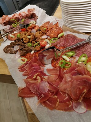 Variedad de carnes y verduras dispuestas sobre una mesa, con una pila de platos blancos al fondo.
