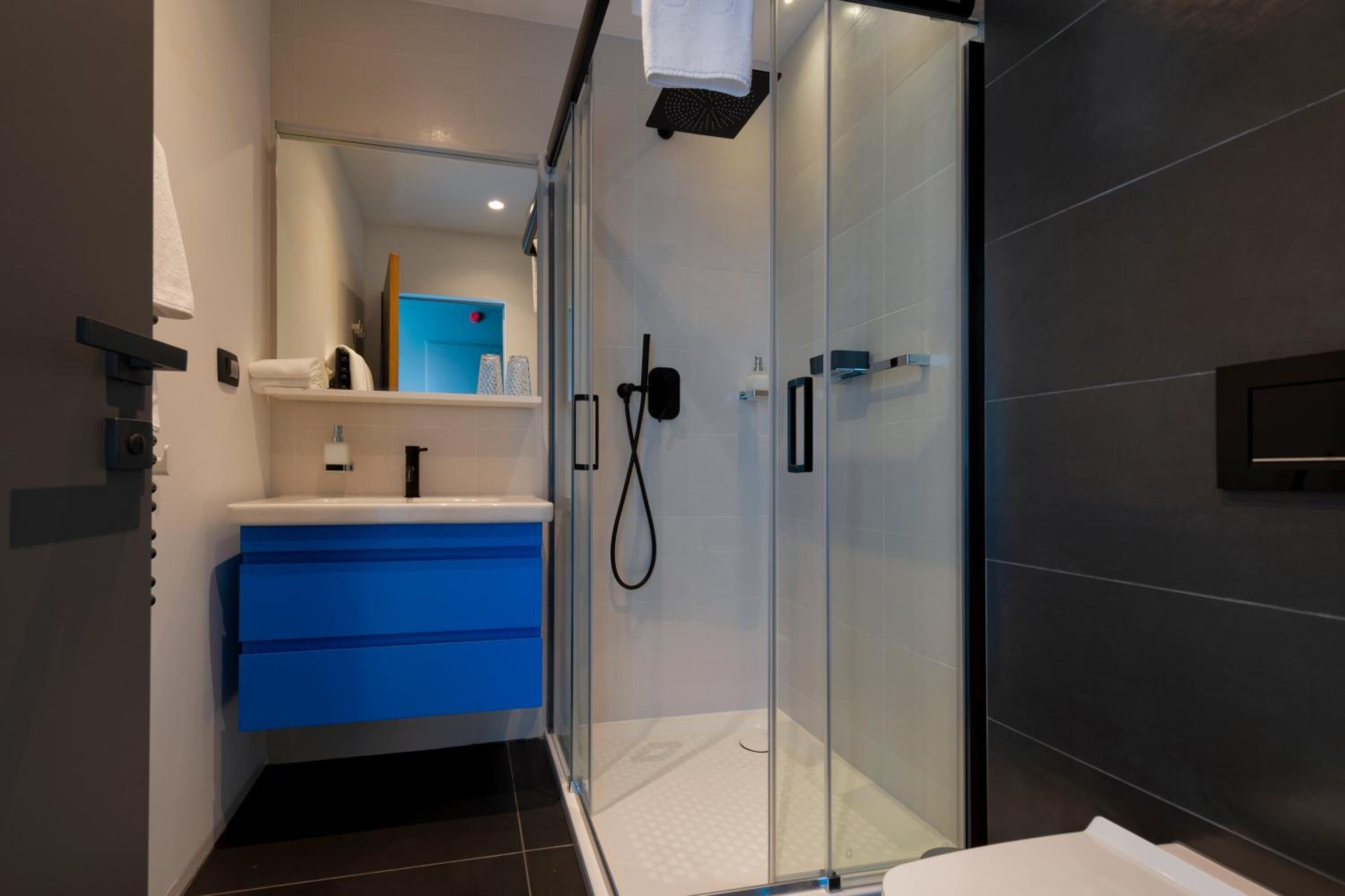 Un baño moderno con cabina de ducha de vidrio, tocador azul y lavamanos blanco.