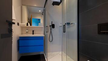 Un baño moderno con cabina de ducha de vidrio, tocador azul y lavamanos blanco.