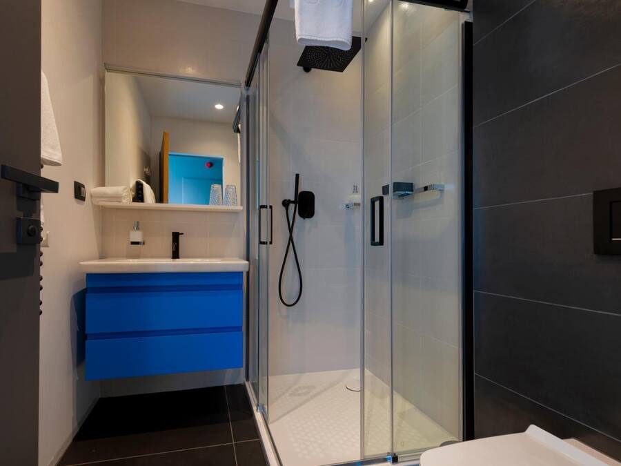 Un baño moderno con cabina de ducha de vidrio, tocador azul y lavamanos blanco.