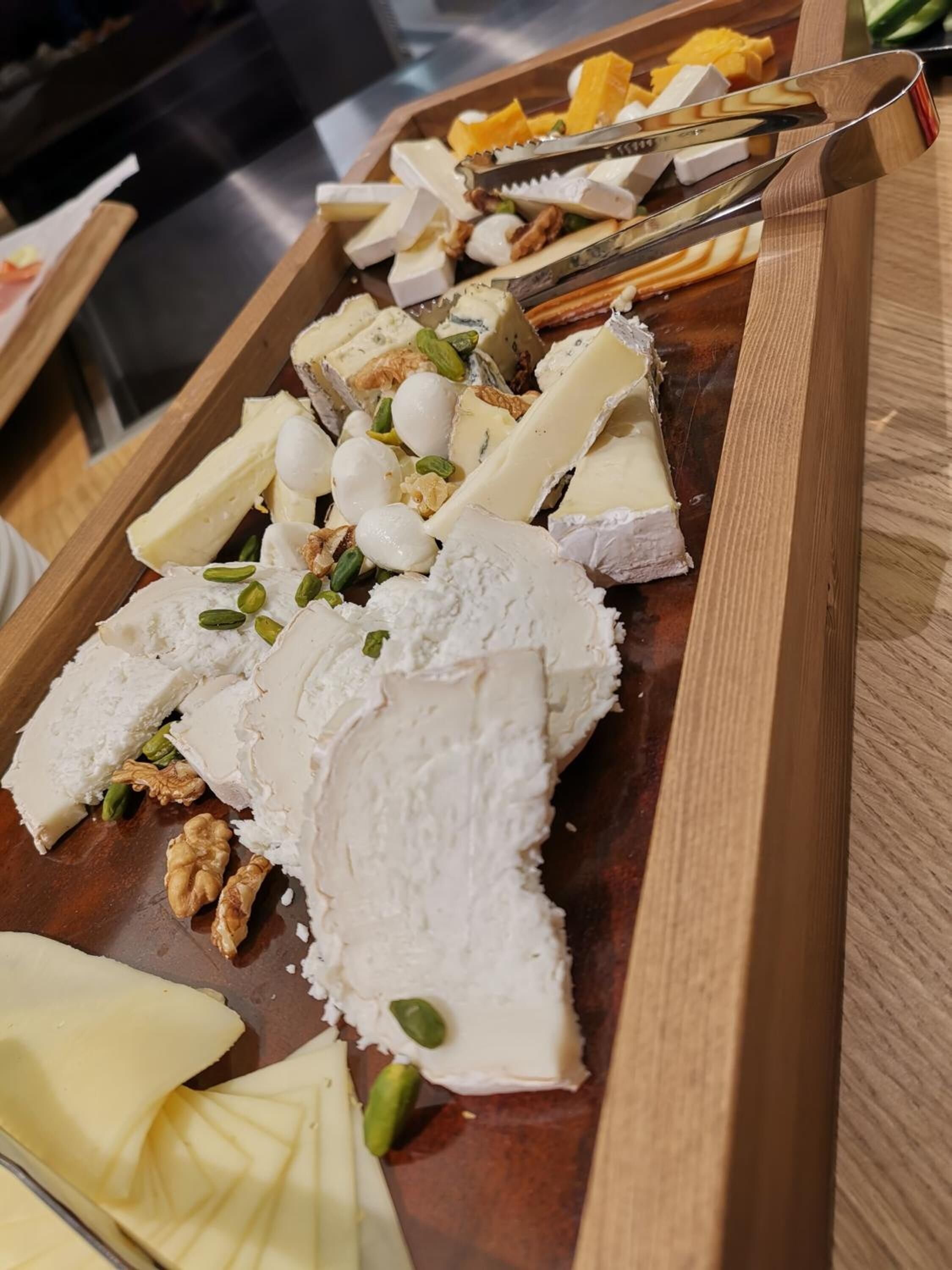A wooden board with various cheeses and nuts.